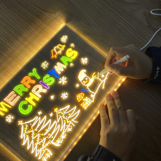 Person writing on LED light-up writing board with Christmas decorations and colorful lights.
