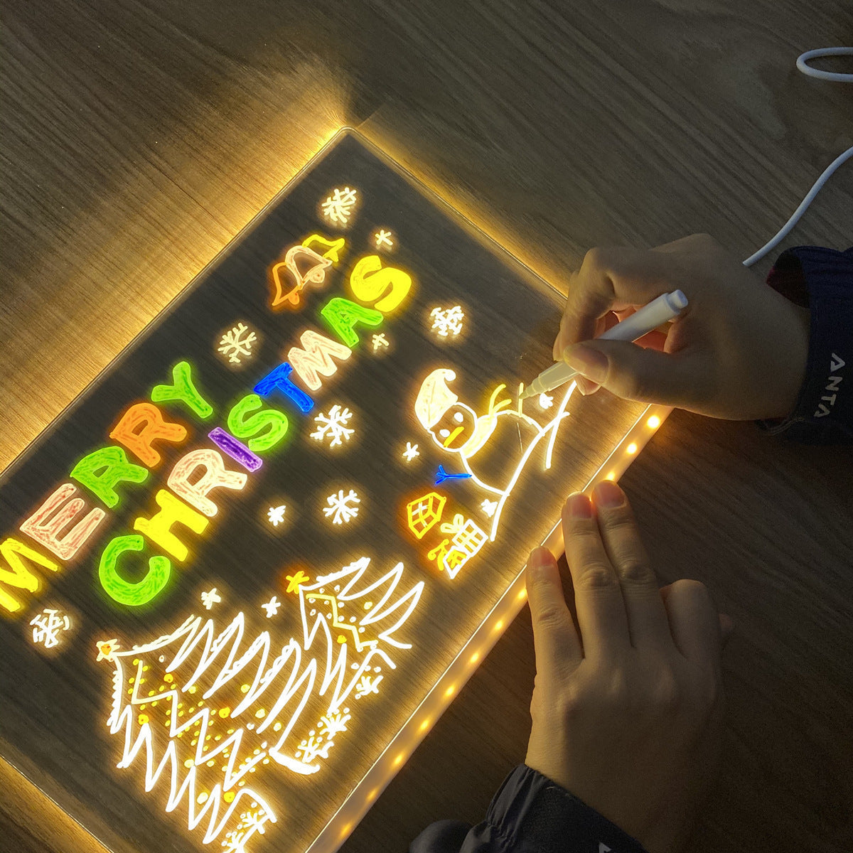 Person writing on LED light-up writing board with Christmas decorations and colorful lights.